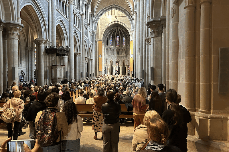Du fond de la cathédrale pleine avec une quinzaine de personne debout et une chorale devant.